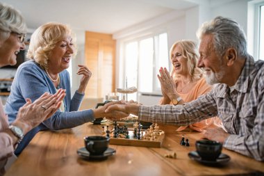 Happy mature woman congratulating to her friend on winning in chess game. 