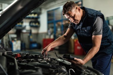 Auto mechanic using diagnostic tool while checking car battery voltage in a workshop. 