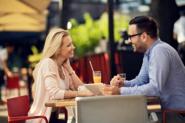 Happy couple talking to each other and having fun while using digital tablet in a cafe. 
