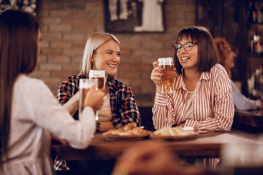 Happy female friends communicating while drinking beer in a bar. 