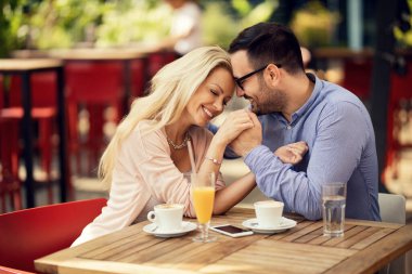Smiling couple in love showing affection to each other while holding hands with their eyes closed in a cafe. 