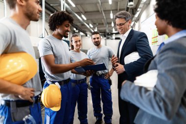 Happy engineer and factory workers going through production reports in industrial plant. 