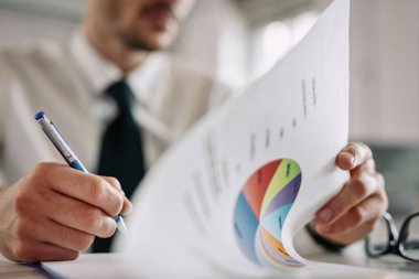Close up of entrepreneur going through business reports and taking notes in the office. 