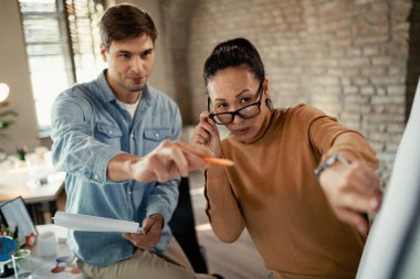 Ofisteki beyaz tahtada iş stratejisini incelerken iş birliği yapan iki girişimci. 