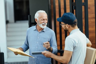 Happy senior man communicating with a deliverer while signing on digital tablet for home delivery. 
