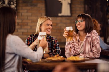 Happy female friends toasting while drinking beer and gathering in a pub. 
