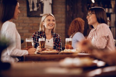 Young happy woman and her friends drinking beer and talking in a bar. 
