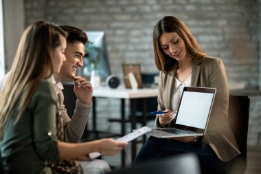Smiling real estate agent using a computer while having a meeting with young couple and making investment plans. 