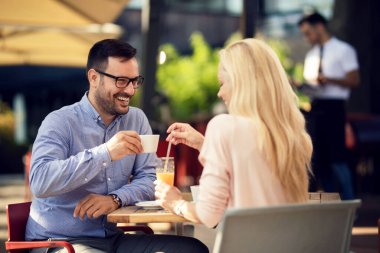 Cheerful couple communicating while relaxing on a date in an outdoor cafe. Focus is on man. 