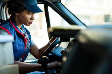Female African American courier staring a mini van while going on package delivery.
