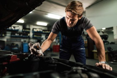 Auto mechanic opening radiator cap while maintaining car cooling system in a workshop. 