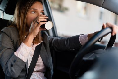 Young businesswoman driving car while drinking takeaway coffee.