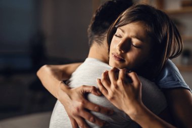 Young crying woman seeking for solace and embracing her boyfriend with eyes closed. 