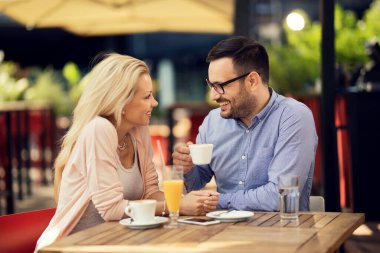 Smiling couple drinking coffee and talking to each other in a cafe. 