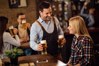 Happy waiter communicating with a woman while serving her beer in a pub. 