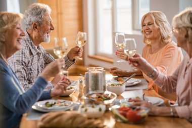 Group of happy senior friends having fun while toasting with wine during lunch time at dining table. 