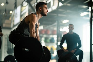 Low angle view of muscular build man doing deadlift while exercising with barbell in a gym. 