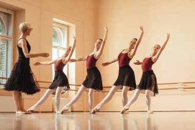 Small group of ballerinas practicing with their mature teacher at ballet studio. 