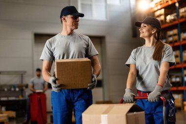 Two happy coworkers communicating while working with packages in distribution warehouse. 