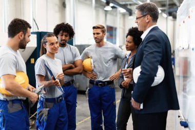 Young engineer talking to corporate managers about production reports while having staff meeting in a factory. 