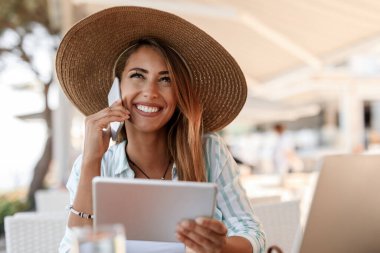 Happy woman using digital tablet and communicating on mobile phone while sitting in a cafe. 