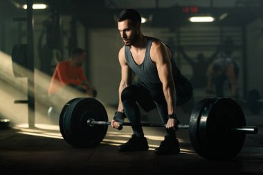 Dedicated sportsman practicing deadlift with barbell during sports training in a gym. There are people in the background. 
