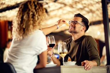 Happy man having fun while girlfriend is feeding him in a restaurant. 