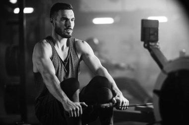 Yong athletic man using rowing machine during sport training n a gym. 