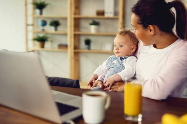 Mother and her baby boy using laptop while relaxing at home. 