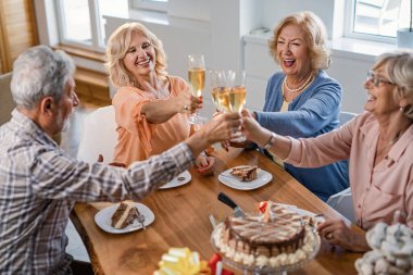 Cheerful seniors toasting with champagne and having fun on a birthday party at home. 