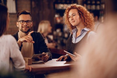 Smiling waitress talking to guests while taking their order in a bar. 