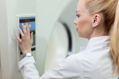 Female doctor pressing buttons and starting MRI scanner at clinic. 