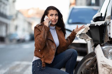 Miserable woman crying while calling for help over mobile phone after a car accident. 