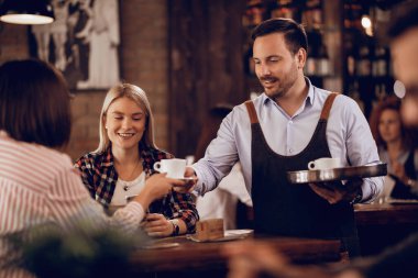Smiling waiter serving coffee to female guests in a cafe. 