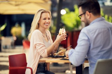 Happy couple talking to each other during lunch time in a restaurant. Focus is on woman eating a sandwich,