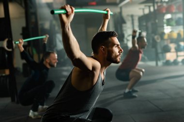 Young sportsmen lifting rod while having strength training in a health club.  Focus is on man in foreground. 