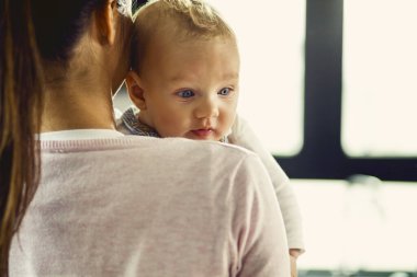 Rear view of mother holding her baby son at home. Focus is on baby. 
