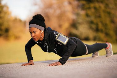 Black sportswoman doing push-ups while exercising in nature. 