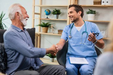 Happy doctor shaking hands with a senior patient while talking to him during home visit. 