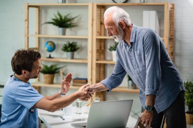 Happy senior man shaking hands with his doctor after medical appointment at clinic. 