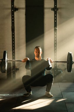 Young athletic man listing barbell while having weight training in health club.