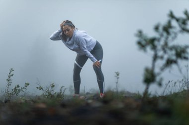 Tired athletic woman taking a break while being out of breath after the run during misty morning. 