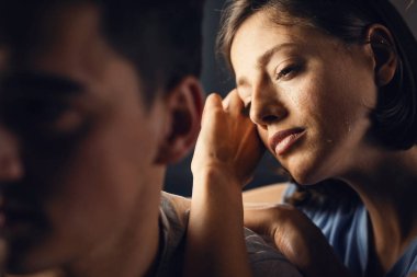 Young sad woman thinking of something while leaning on boyfriend's shoulder and crying. 