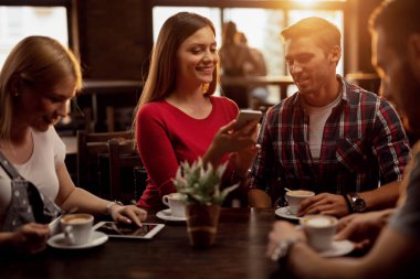 Group of friends using wireless technology while gathering in a cafe. Focus is on couple using mobile phone together. 