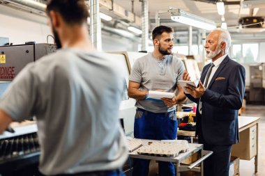 Mature company manager communicating with manual worker while visiting a factory. Focus is on young man. 