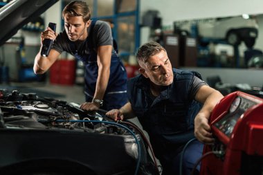 Two mechanics maintaining air conditioning unit of a car at auto repair workshop. 