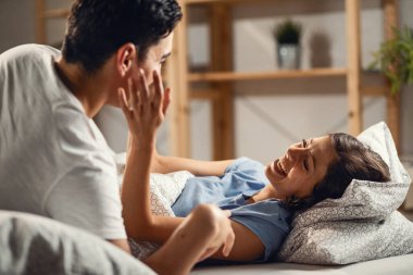 Young couple having fun and laughing while relaxing on the bed. Focus is on woman. 