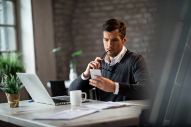 Serious businessman working in the office and text messaging on smart phone.