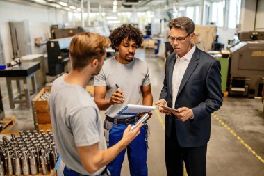 African American worker and his colleagues doing quality control check of manufactured products with their manager in industrial building. 