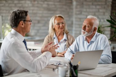 Mature couple meeting bank manager and communicating with him during consultations in the office. 